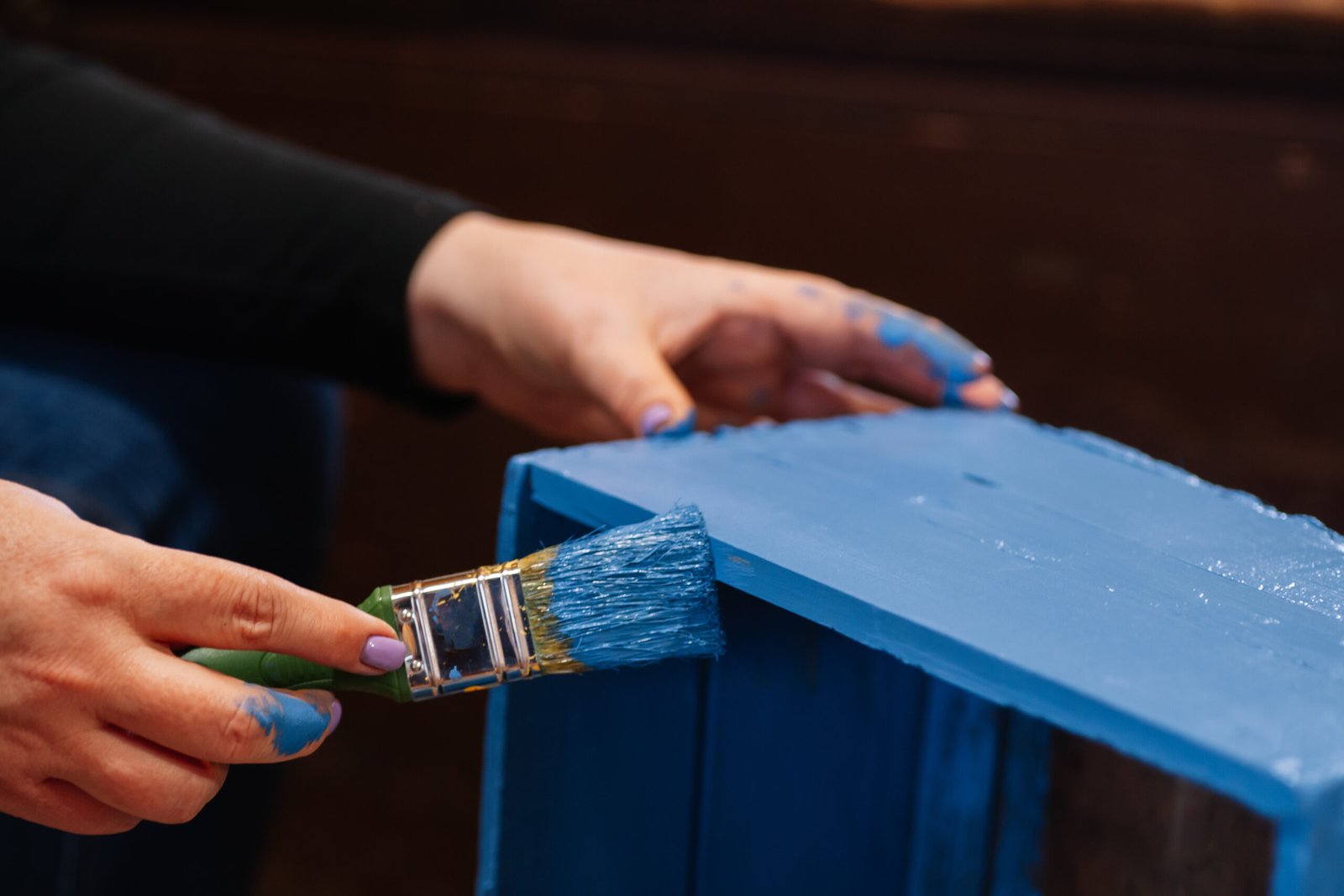 Closeup of big brush in stained hands coating closet drawer made of wood in blue color. Reuse of old things. Sustainable eco-friendly actions for planet future.