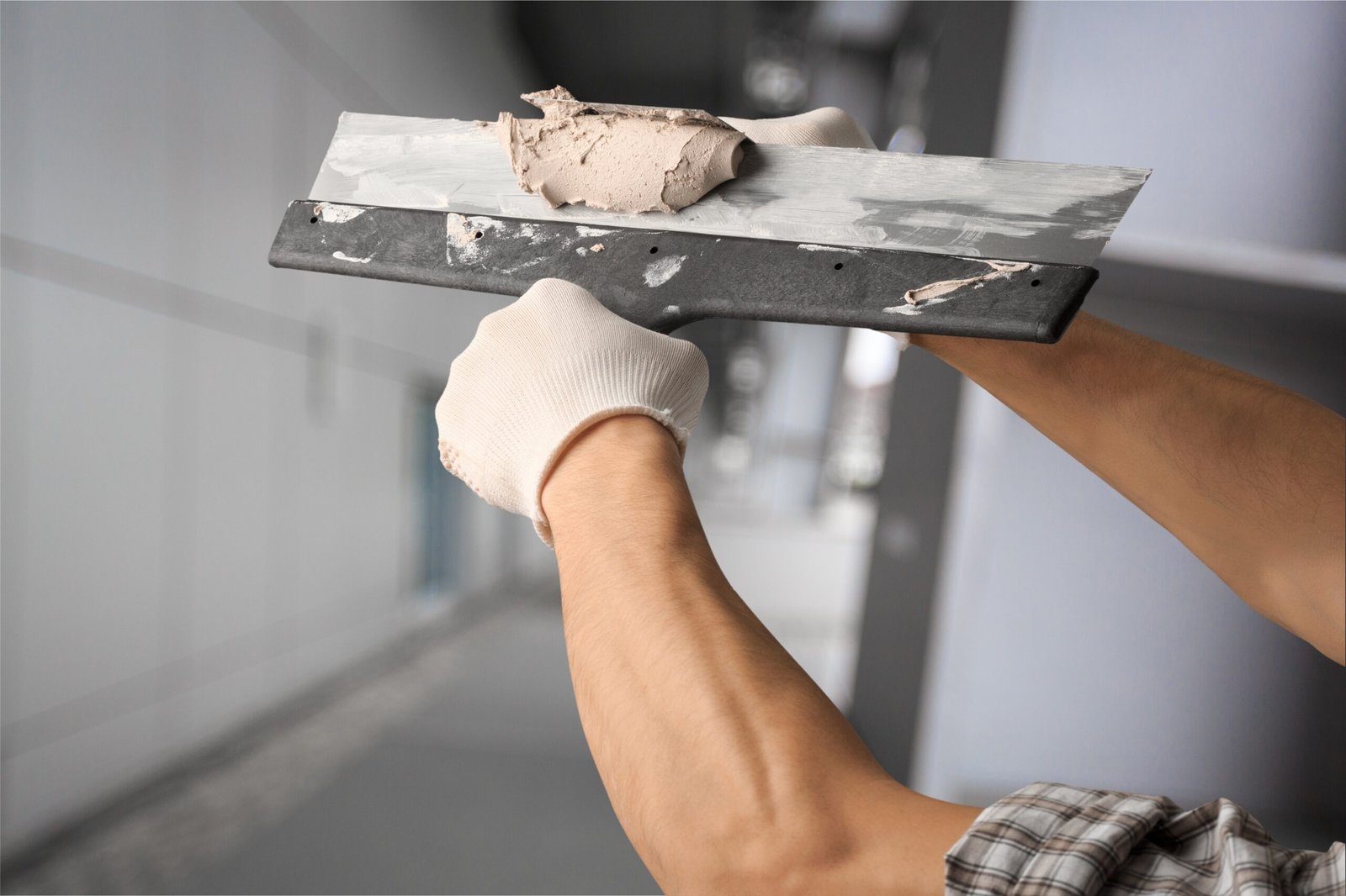 Thirty years old manual worker with wall plastering tools renovating house.